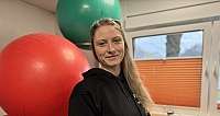 Junge Frau in schwarzem Hoodie vor großen roten und grünen Gymnastikbällen in Raum