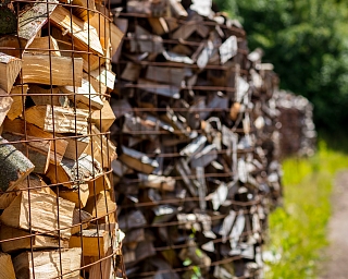Holzscheite in einem Drahtkorb, im Hintergrund weitere Holzstapel.