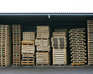 Lager mit mehreren gestapelten Holzpaletten unter einem Dach.