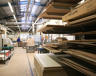 Innenansicht einer Holzwerkstatt mit Holzplatten und Maschinen.