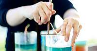 Person taucht Docht in ein Glas mit blauer Flüssigkeit zur Kerzenherstellung