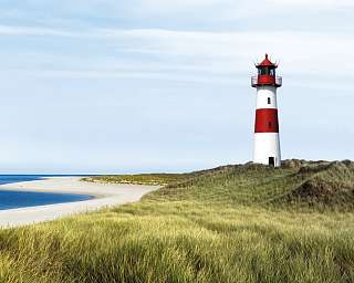 Ein roter und weißer Leuchtturm neben einem Sandstrand und Meer.