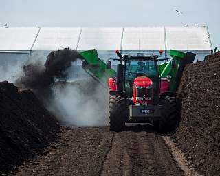Ein roter Traktor verteilt Kompost zwischen zwei Erdhügeln.