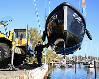 Ein Mann hebt ein Boot mit einem Kran am Hafen an.