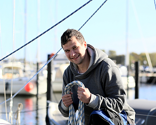 Mann hält ein Seil und lächelt am Bootsanleger.