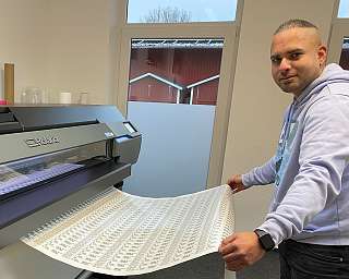 Ein Mann bedient einen großen Drucker mit bedrucktem Papier.