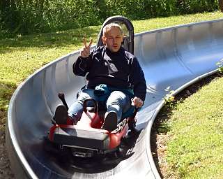 Ein Mann fährt auf einer Rodelbahn und zeigt das Peace-Zeichen.