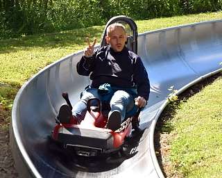 Ein Mann fährt auf einer Rodelbahn und zeigt das Peace-Zeichen.