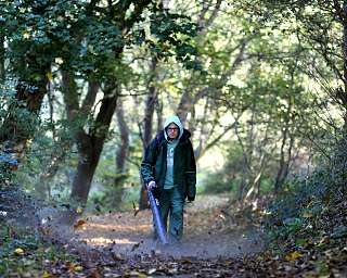 Person nutzt einen Laubbläser auf einem Waldweg.