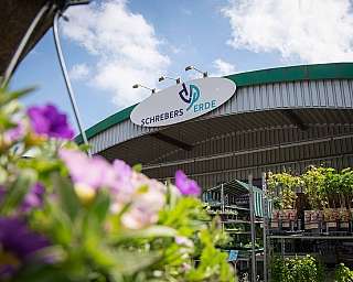 Verkaufsstand mit Pflanzen und Gartenzubehör unter einem Dach mit Schild Schrebenspieler Erde
