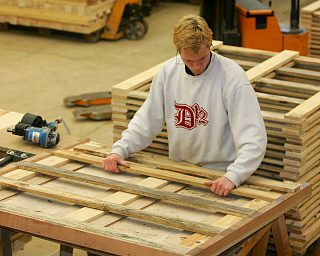 Ein Mann montiert Holzlatten auf einem Tisch in einer Werkstatt.
