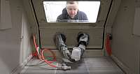Mann arbeitet in einer Sandstrahlkabine mit Handschuhen.