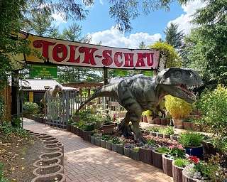 Große Dinosaurierstatue neben einem Tor mit Schild "Tolk-Schau" im Park