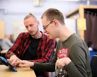 Zwei Personen interagieren mit einem Tablet in einem Lernumfeld.