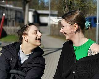 Zwei Frauen lachen und schauen sich an, im Hintergrund ein Spielplatz.