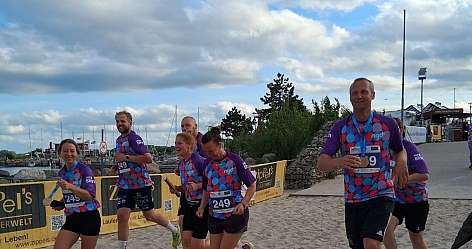Sieben Läufer in bunten Shirts laufen am Sandstrand bei bewölktem Himmel
