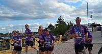 Sieben Läufer in bunten Shirts laufen am Sandstrand bei bewölktem Himmel
