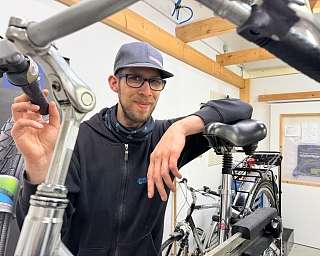 Mann mit Brille und Mütze repariert Fahrrad in einer Werkstatt