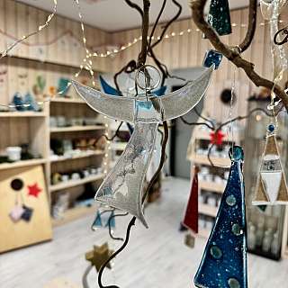 Nahaufnahme einer Glas-Engel-Dekoration in einem Raum mit Holzregalen und Lichterketten