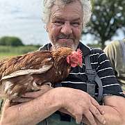 Ein älterer Mann hält ein Huhn in den Armen und lächelt.