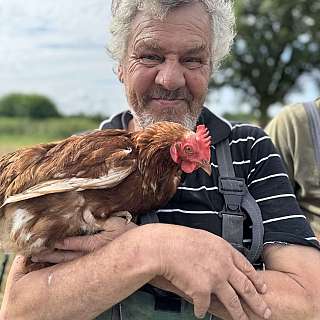 Ein älterer Mann hält ein Huhn in den Armen und lächelt.