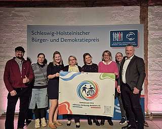 Gruppe von Personen mit Banner bei Preisverleihung in Schleswig-Holstein.