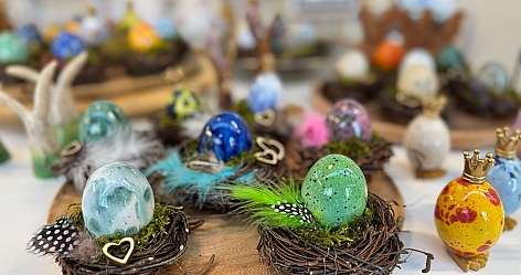 Bunte dekorative Ostereier in kleinen Nestern mit Federn auf einem Holzteller