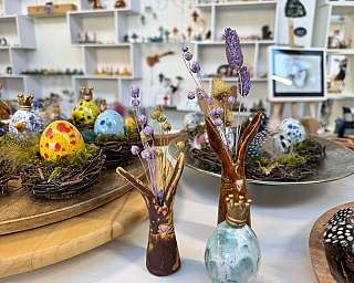 Bunte bemalte Ostereier in Nestern und kleine Vasen mit Trockenblumen auf einem Tisch